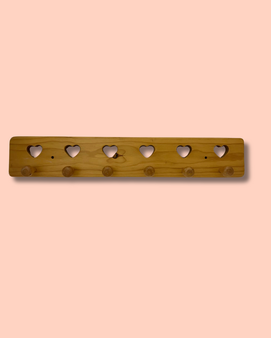 Wooden wall hook with heart-shaped holes on a peach background