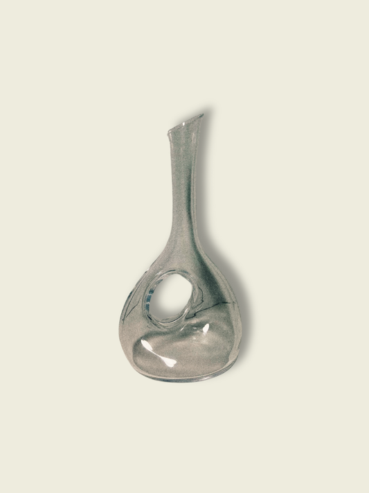 A clear crystal round wine decanter against a beige background.