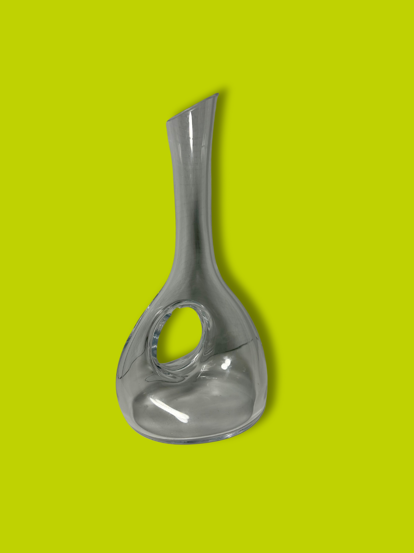 A clear crystal round wine decanter against a green background.