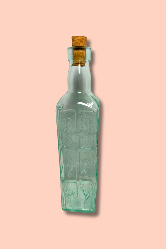 Green glass bottle with a cork on a pink background