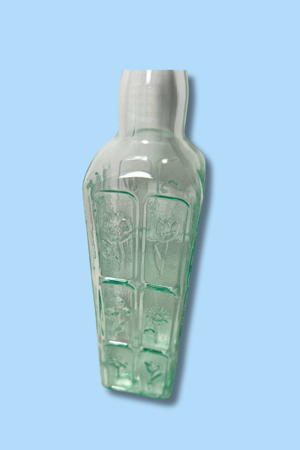 Decorative glass bottle with embossed design on a light blue background