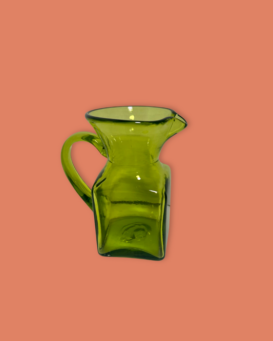 Green glass pitcher on a peach background