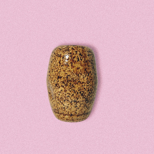 A handmade ceramic brown speckled jar on a pink background.