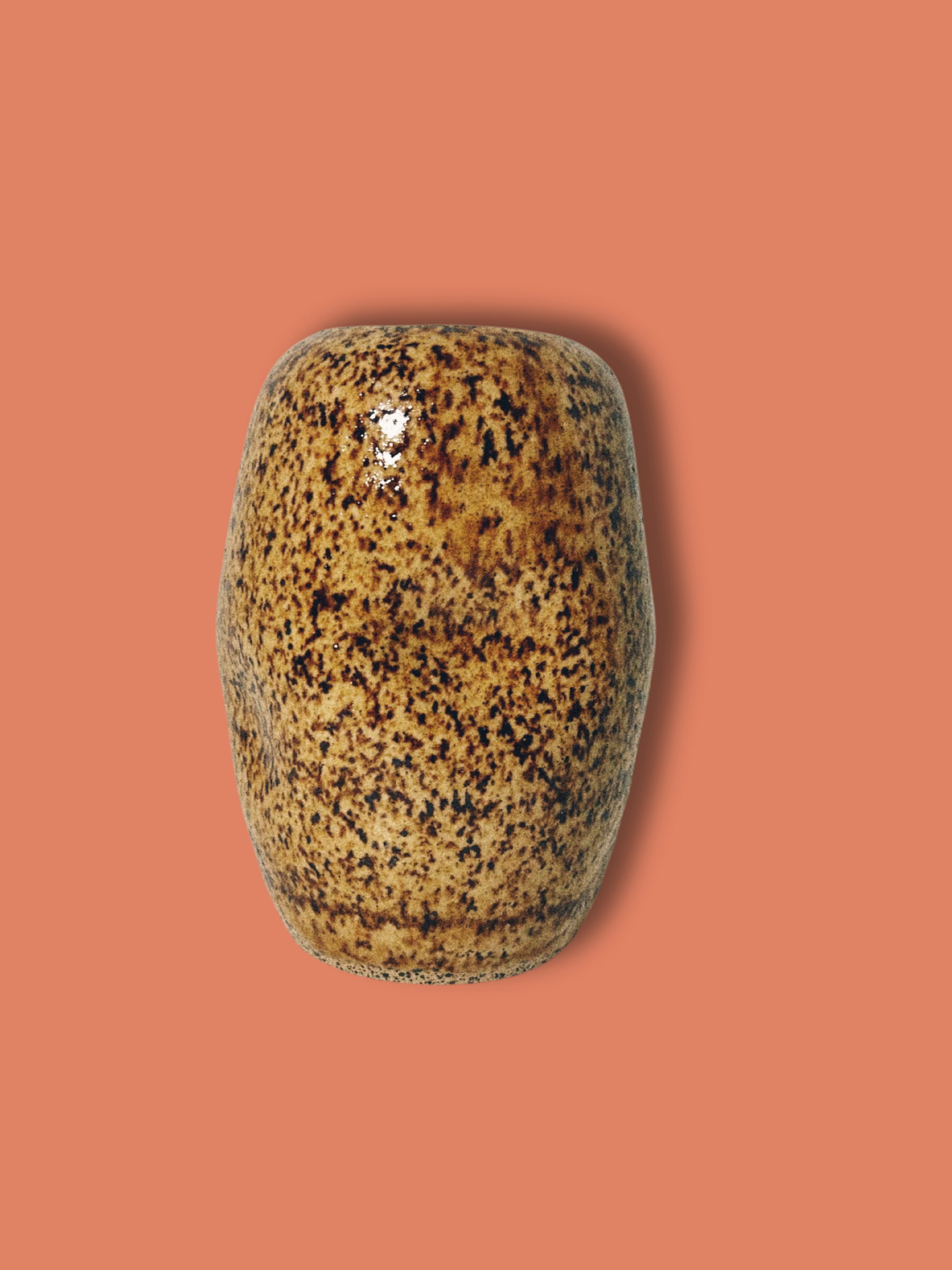 A handmade ceramic brown speckled jar on an orange background.