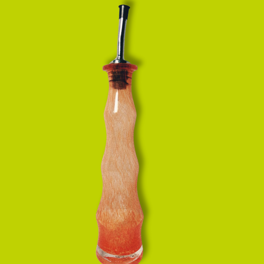 A clear handblown glass olive oil cruet with an orange tint against a bright green background.