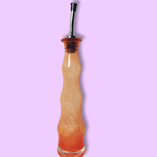 A clear handblown glass olive oil cruet with an orange tint against a purple background.