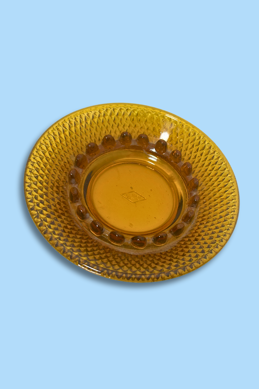 Amber glass ashtray with textured rim on a light blue background
