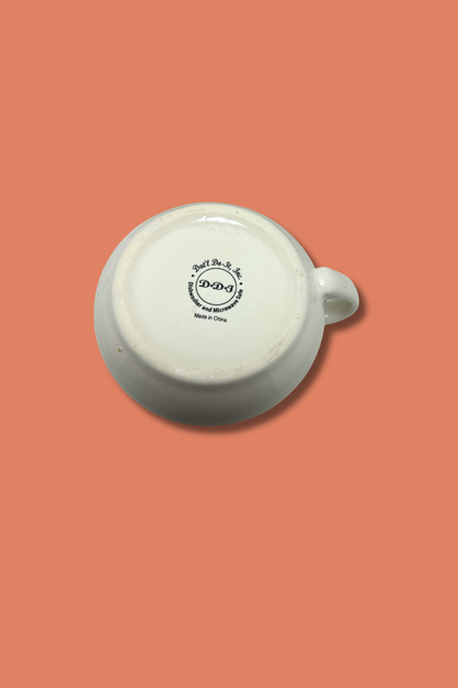White ceramic mug with a logo on a peach background