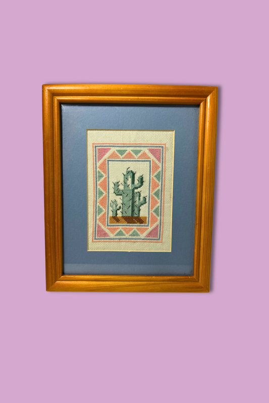 Framed cross-stitched picture of a cactus on a purple wall