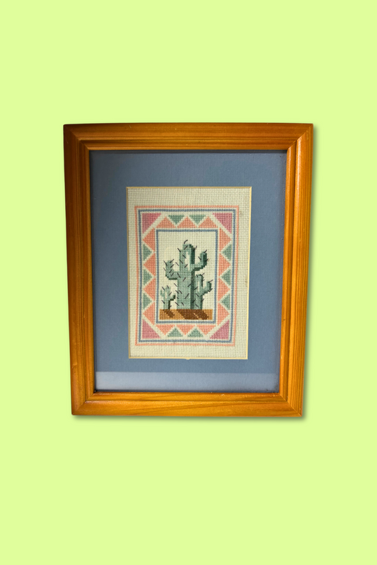 Framed cross-stitched picture of a cactus on a light green wall