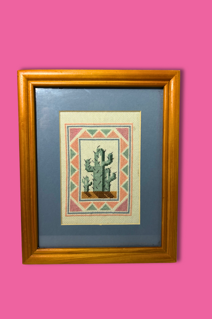 Framed cross-stitched picture of a cactus on a pink background