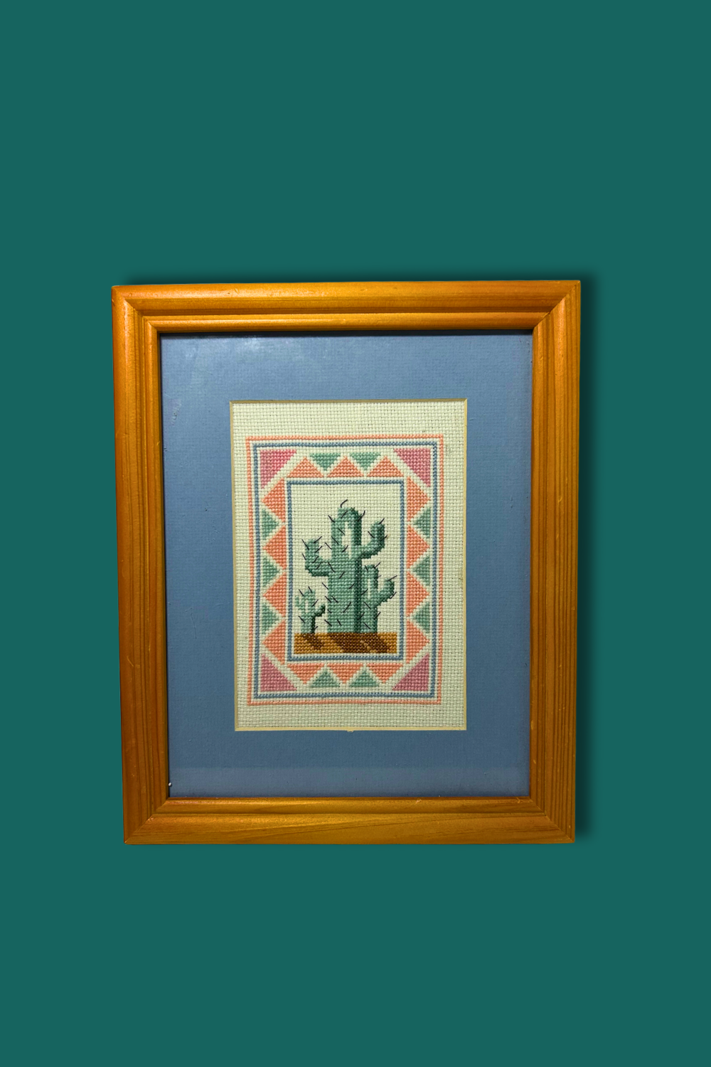 Framed cross-stitched picture of a cactus on a blue background