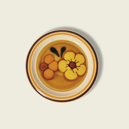 A vintage salad plate with a floral pattern in yellow, orange, and black colors, with a white rim.