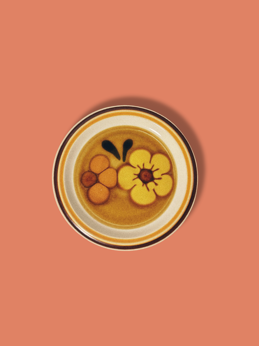 A vintage salad plate with a floral pattern in yellow, orange, and black colors, with a white rim.
