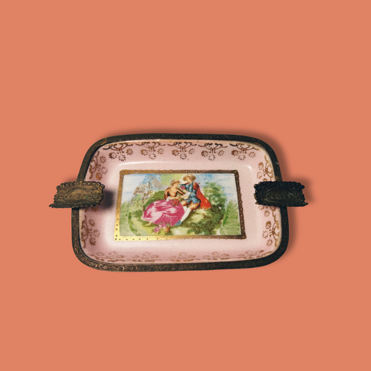 A vintage handpainted porcelain ashtray with brass accents and a floral design, featuring a central picture of a woman.