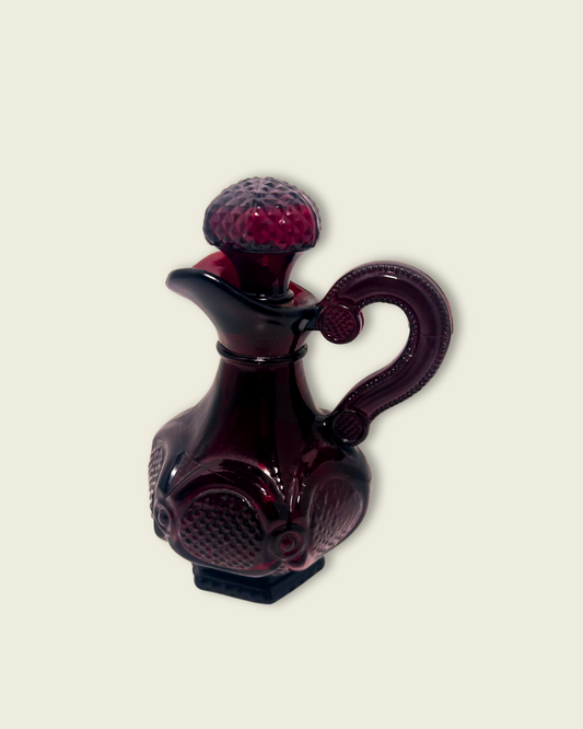 A ruby glass ewer with a textured top on a beige background