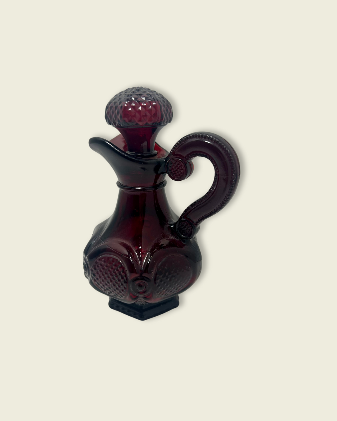 Dark red glass pitcher with a textured handle on a beige background