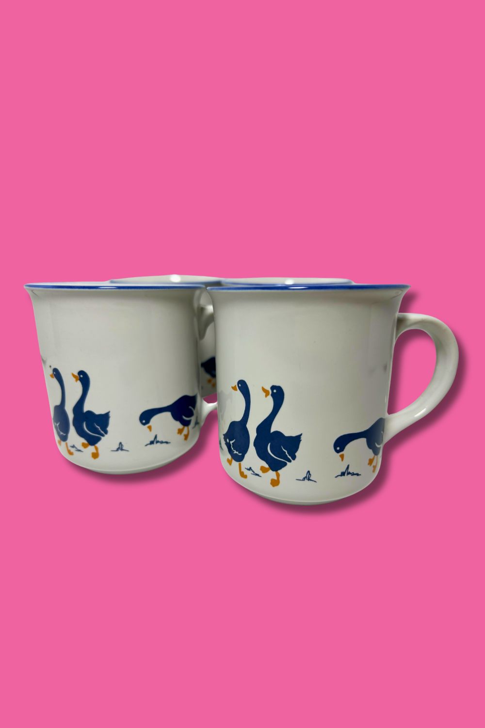 Two mugs with blue goose designs on a pink background