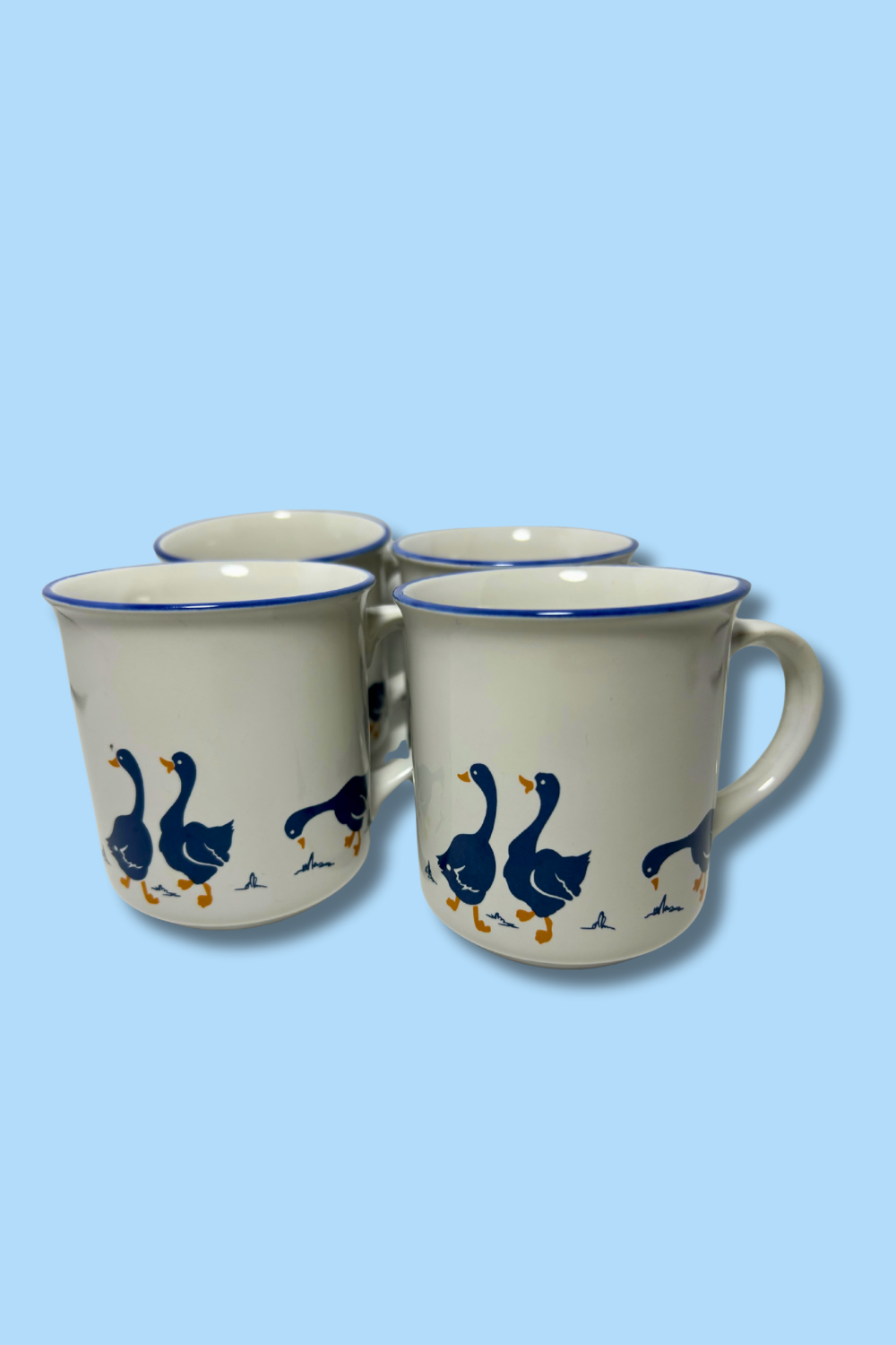 Four ceramic mugs with goose design on a light blue background