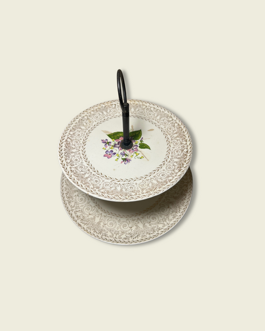 Two-tiered ceramic cake stand with floral design on a beige background