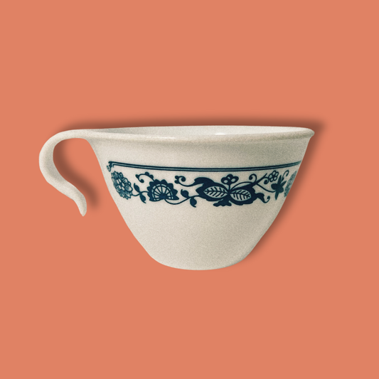 A white ceramic tea cup with a blue floral pattern and a hook handle, against an orange background.