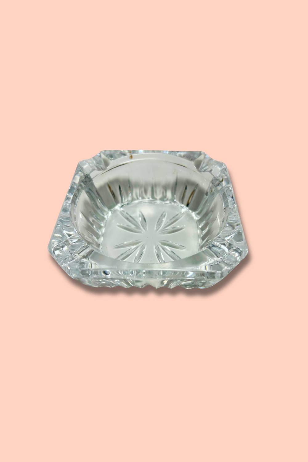 Clear crystal ashtray with starburst pattern on a pink background