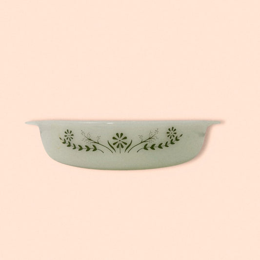 A white glass baking dish with a green daisy pattern on the exterior, displayed against a pink background.