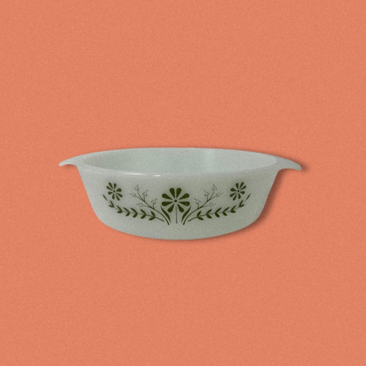 A vintage Glasbake green baking dish with a daisy pattern on the front, displayed against an orange background.
