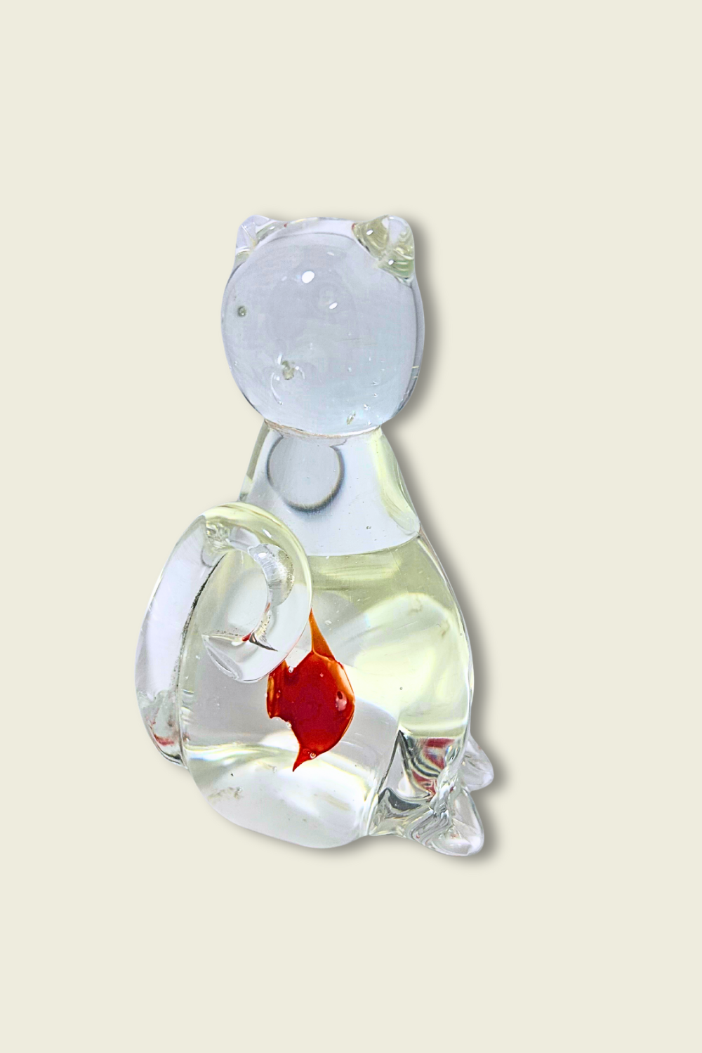 Glass sculpture of a cat with a fish bowl on a beige background