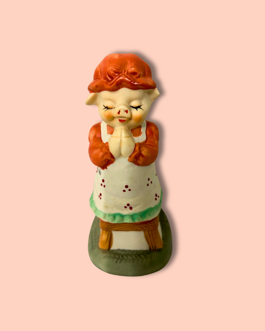 Vintage-style pig figurine with a red hat and white dress on a pink background