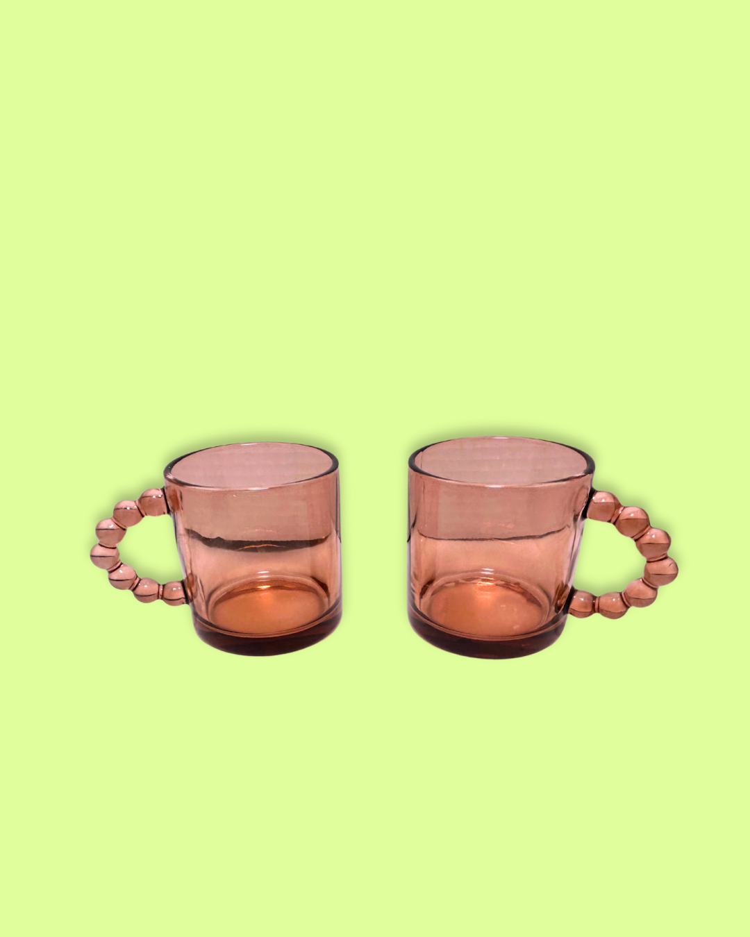 A pair of pink glass mugs with beaded handles on a green background.