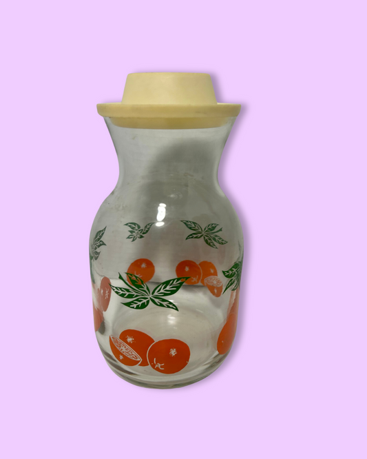 Glass jar with a wooden lid featuring orange illustrations on a light purple background