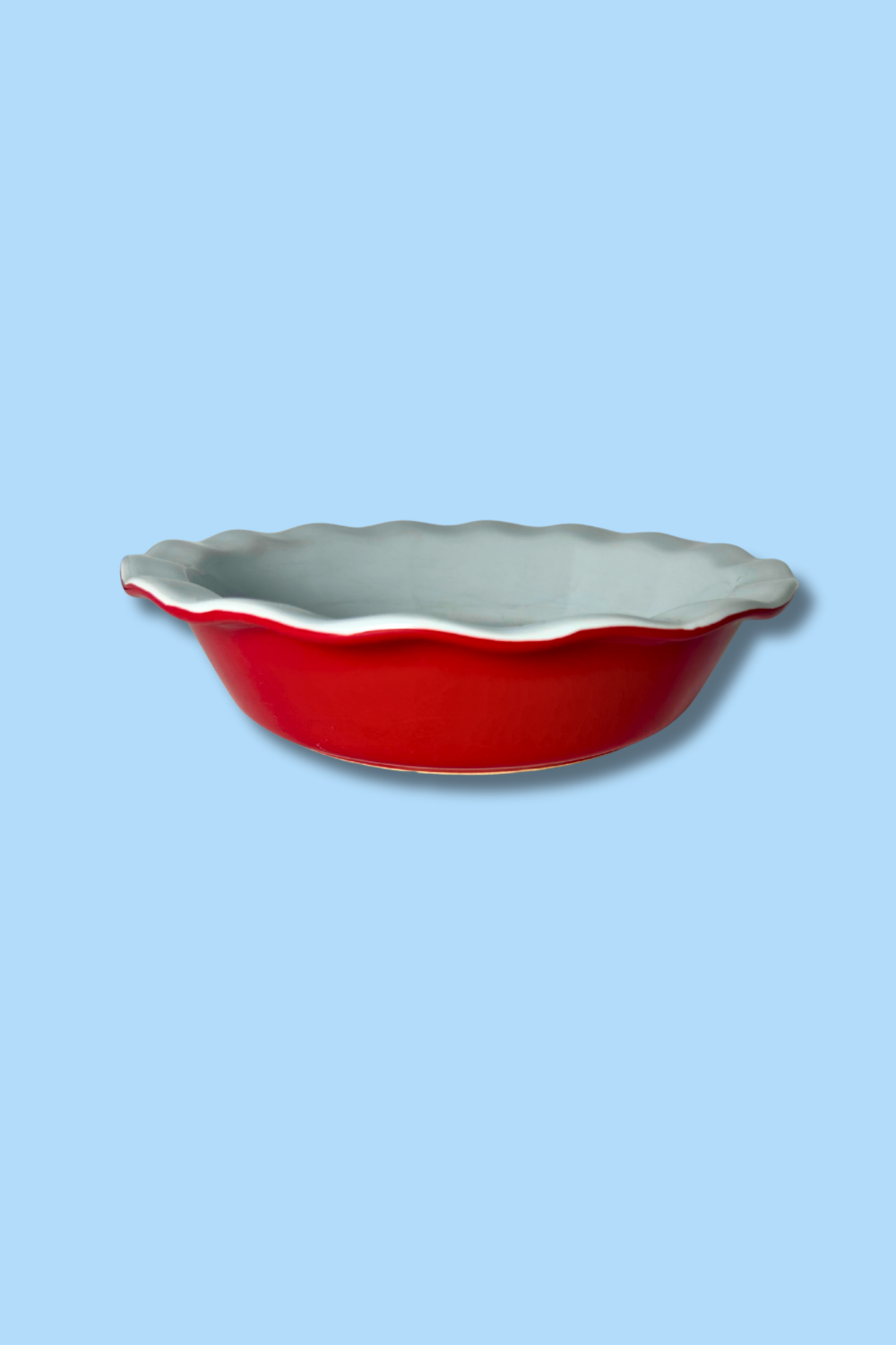 Red ceramic pie dish with scalloped edge on a light blue background