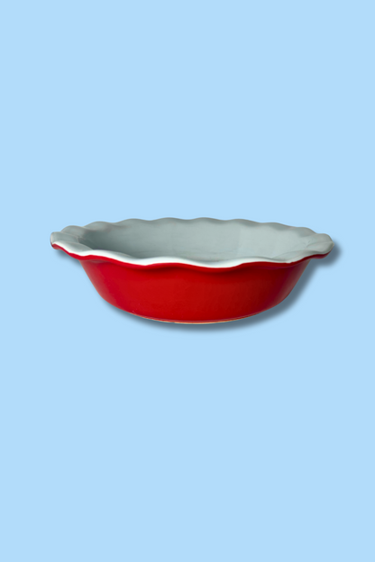 Red ceramic pie dish with scalloped edge on a light blue background