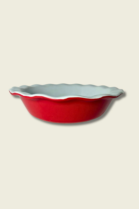 Red ceramic pie dish with scalloped edge on a beige background