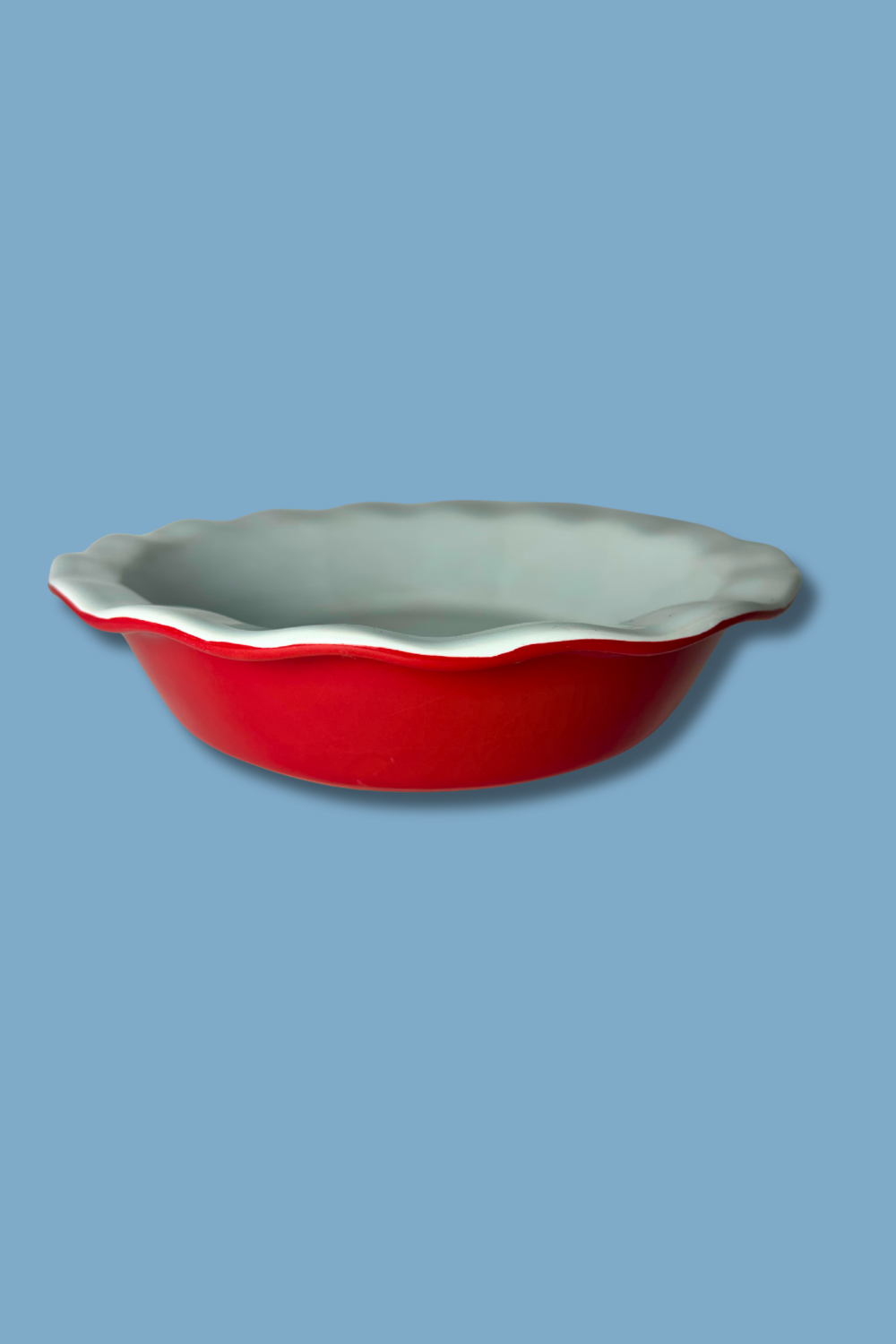 Red ceramic pie dish with a scalloped edge on a blue background