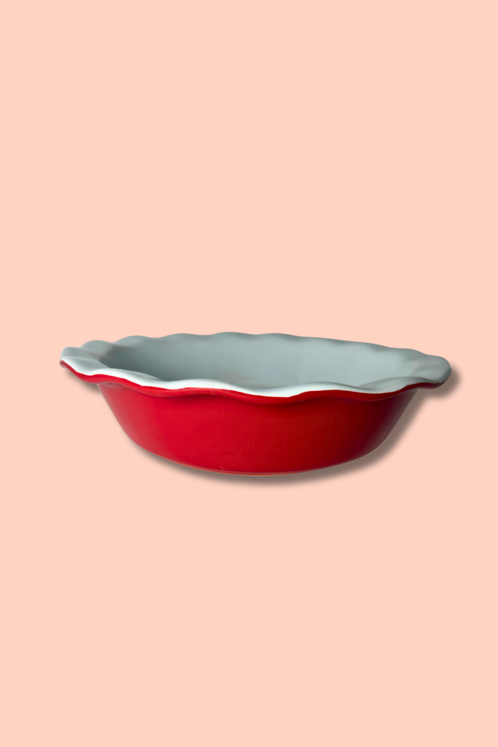 Red ceramic pie dish with scalloped edge on a pink background
