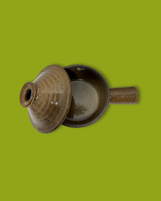 A brown handmade ceramic soup crock with a handle, isolated on a green background.